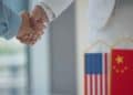 vemos una imagen que representa las noticias de china y estados unidos con dos manos estrechandose delante de dos banderas