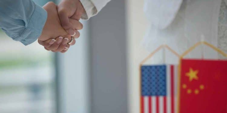 vemos una imagen que representa las noticias de china y estados unidos con dos manos estrechandose delante de dos banderas