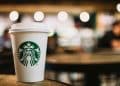 vemos una imagen de la empresa starbucks con un vaso que contiene su logo y de fondo una de sus cafeterias