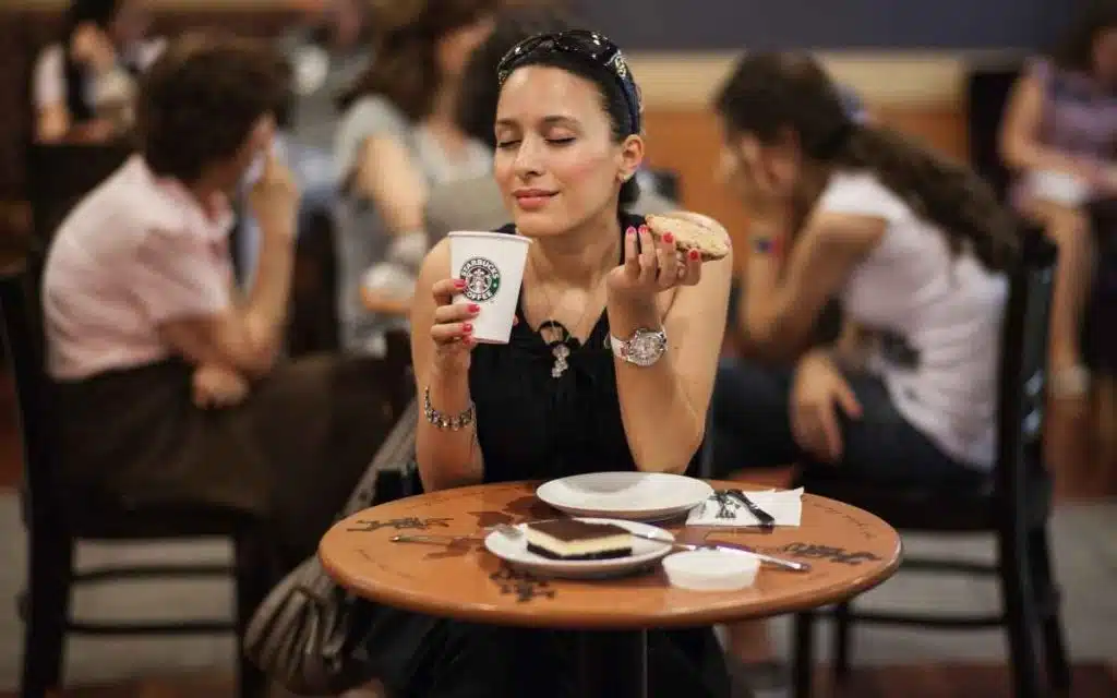 Vemos una imagen de la empresa starbucks con una mujer en uno de los cafes de la marca disfrutando de una bebida y una galleta