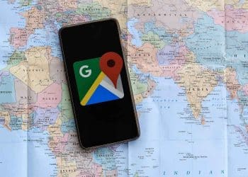 Vemos por qué no aparece mi negocio en google maps con una imagen de un celular con la app google maps sobre un mapa mundial de papel.