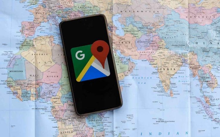 Vemos por qué no aparece mi negocio en google maps con una imagen de un celular con la app google maps sobre un mapa mundial de papel.