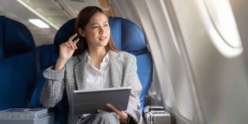 Vemos una imagen de una mujer sentada con una computadora en un avión, referido a negocios para ser millonario