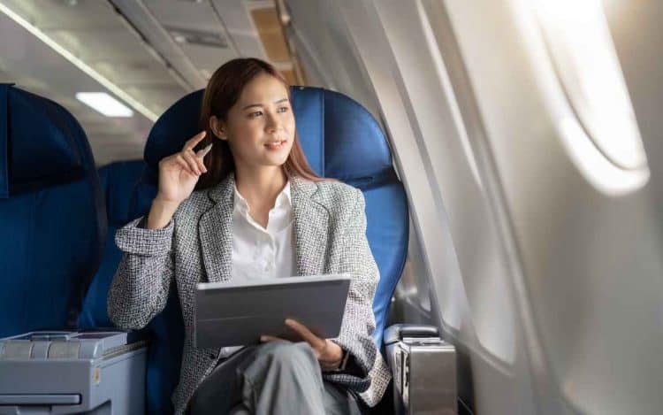 Vemos una imagen de una mujer sentada con una computadora en un avión, referido a negocios para ser millonario