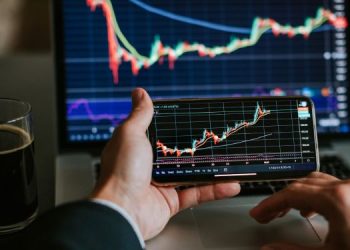 Vemos una imagen de alguien revisando el mercado de acciones 2023 en su computadora y celular.