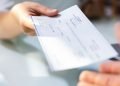 Vemos una persona entregando un cheque a otra, en referencia a cómo hacer una nómina de pago.