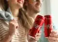 Vemos una imagen de una pareja sosteniendo unas latas de Coca Cola, en relación con la historia de la publicidad de Coca Cola.
