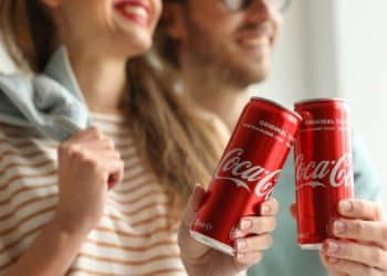 Vemos una imagen de una pareja sosteniendo unas latas de Coca Cola, en relación con la historia de la publicidad de Coca Cola.