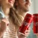 Vemos una imagen de una pareja sosteniendo unas latas de Coca Cola, en relación con la historia de la publicidad de Coca Cola.