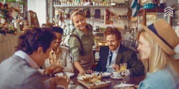 Vemos una imagen de una persona sirviendo a un grupo de personas en un pequeño restaurante, en referencia a cómo emprender un negocio de comida.