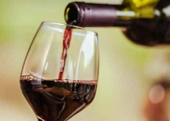 Vemos una copa de vidrio siendo llenada por una botella de vino, en referencia al estudio de mercado de vinos en el Perú.