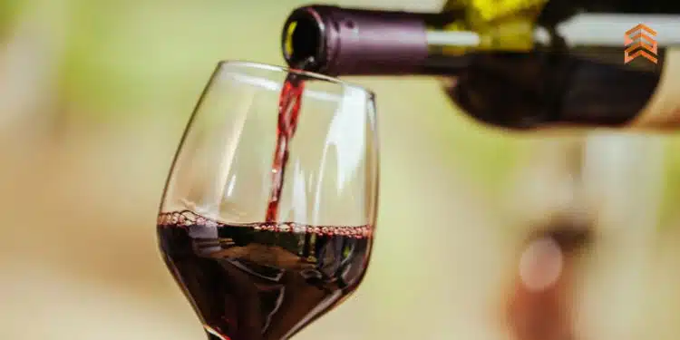 Vemos una copa de vidrio siendo llenada por una botella de vino, en referencia al estudio de mercado de vinos en el Perú.