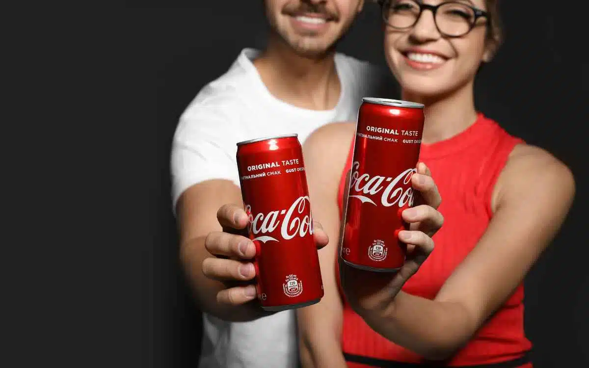 Vemos dos personas sosteniendo latas de Coca Cola, en referencia a la misión y visión de Coca Cola.
