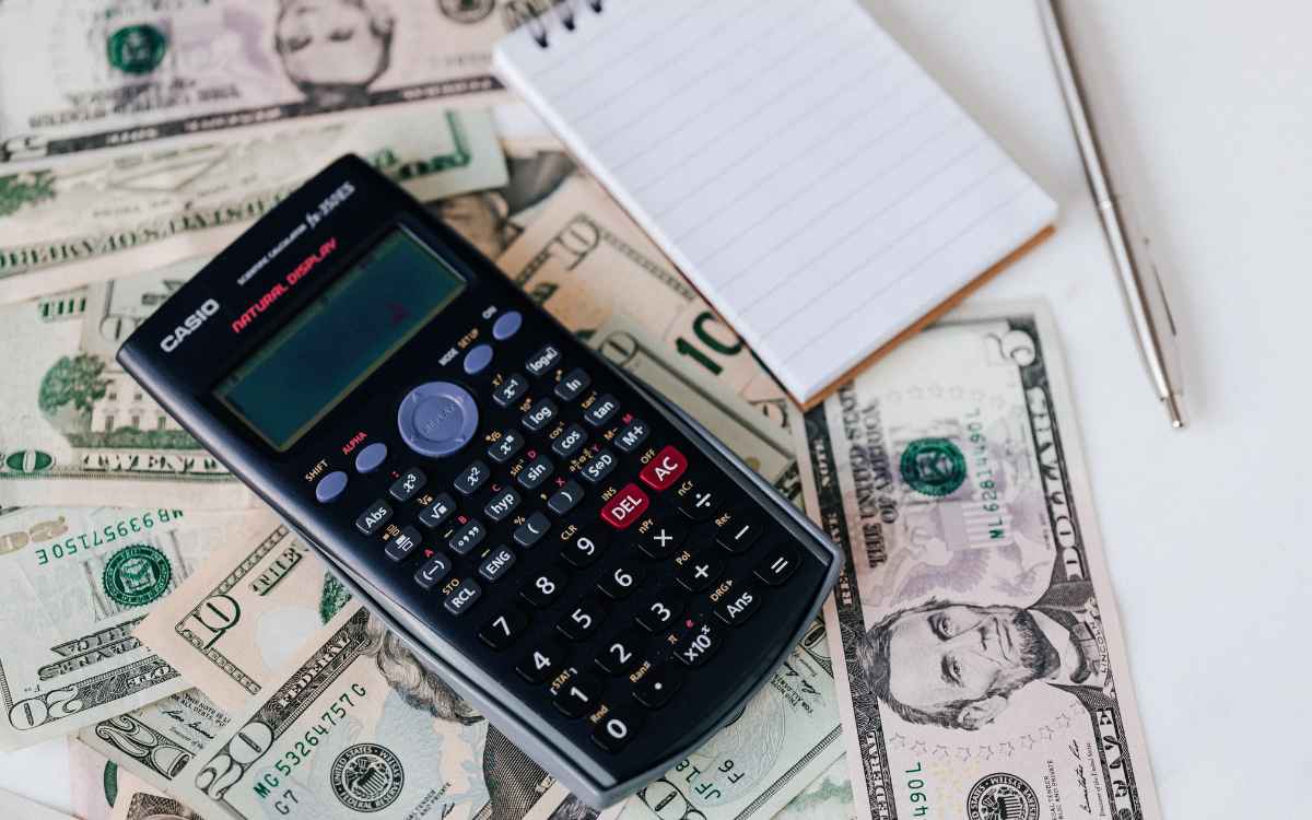Vemos una imagen de una calculadora sobre billetes y documentos, en referencia a la elaboración de un presupuesto de ventas. 