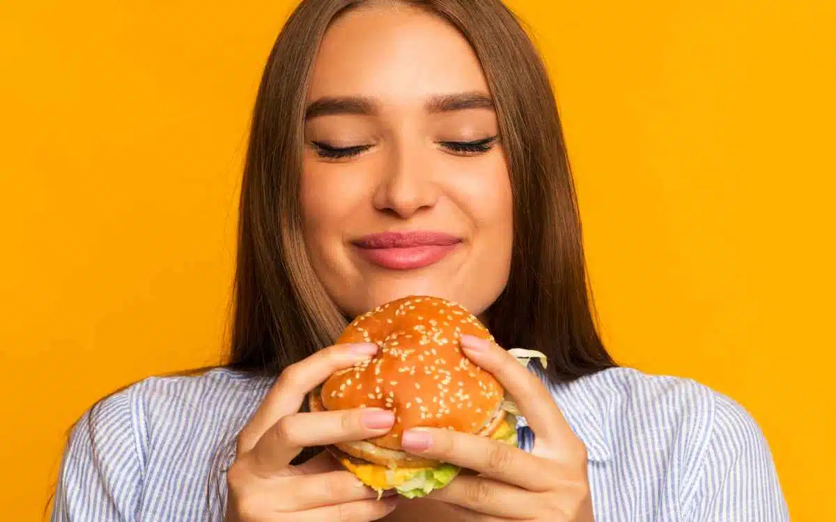 Imagen de una mujer comiendo una hamburguesa, en referencia a los nombres para negocios de hamburguesas.