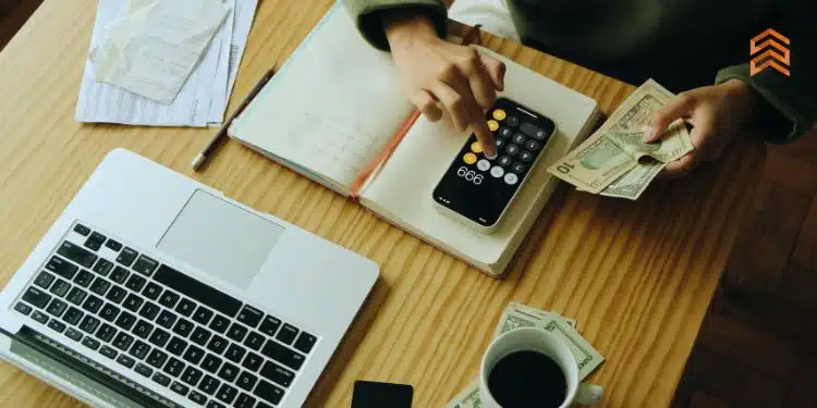 Vemos una imagen de una persona realizando cálculos con un celular y una computadora, en referencia a las diferentes fuentes de financiación internas que existen.