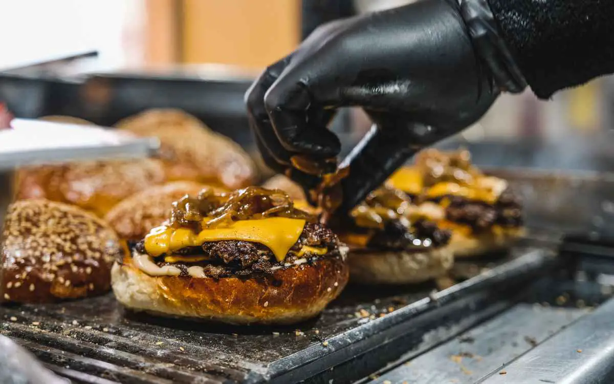 Imagen de una persona preparando hamburguesas en una parrilla, en relación con los nombres para negocios de hamburguesas.