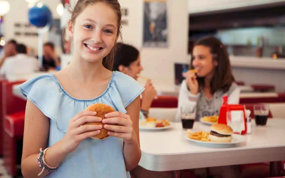 Imagen de una niña comiendo una hamburguesa en un restaurante familiar, en referencia a la búsqueda de nombres para negocios de hamburguesas.
