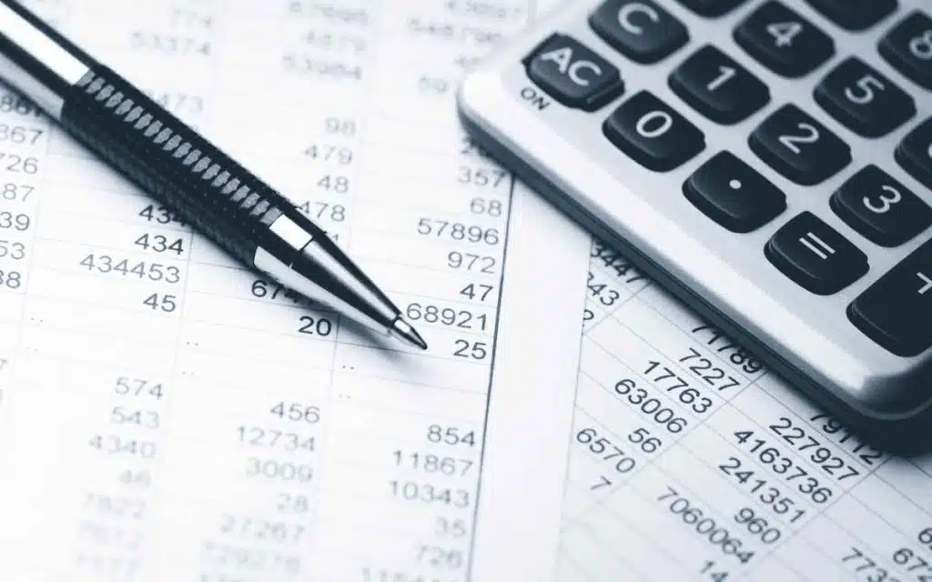 Vemos una imagen de diferentes tipos de balances contables en papel, acompañados de una lapicera y una calculadora. 