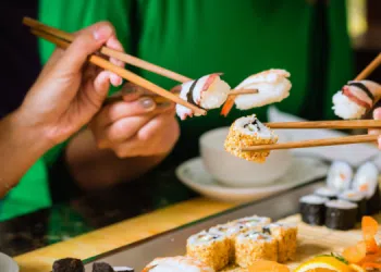 Vemos una imagen de personas comiendo sushi con palillos, en referencia a la búsqueda de nombres para sushi restaurant.
