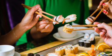 Vemos una imagen de personas comiendo sushi con palillos, en referencia a la búsqueda de nombres para sushi restaurant.