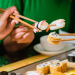 Vemos una imagen de personas comiendo sushi con palillos, en referencia a la búsqueda de nombres para sushi restaurant.