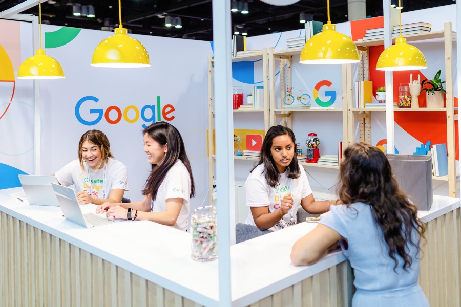 Vemos tres empleadas de Google atendiendo un stand en un evento de la empresa, en relación con la cultura y el organigrama de Google.