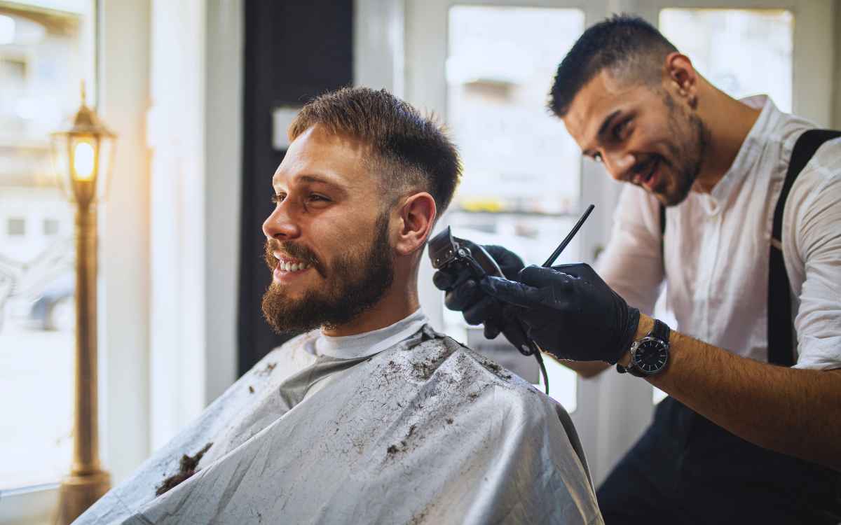 Vemos un barbero prestando servicios a un cliente, en relación con la búsqueda de nombres de barberías.