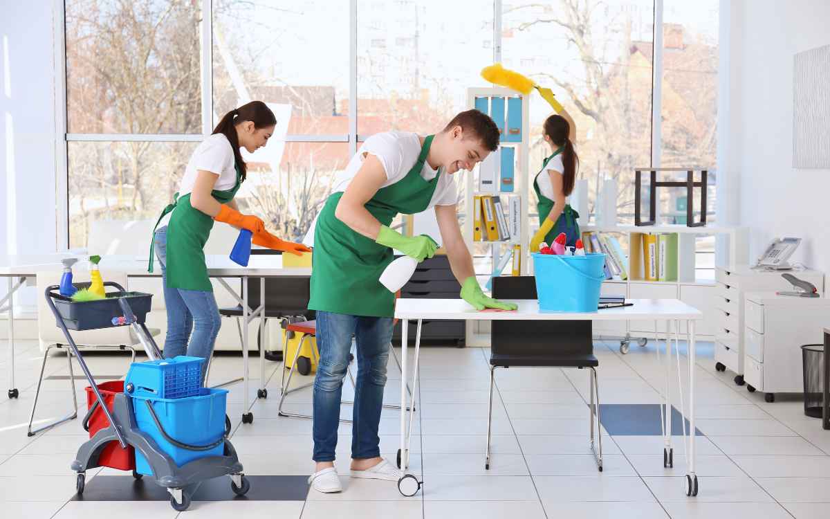 Vemos tres personas de una empresa de limpieza realizando sus tareas en una oficina.