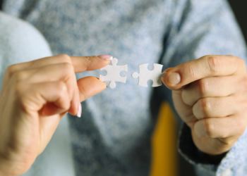 Vemos dos personas uniendo dos piezas de un rompecabezas, en relación con la aplicación de PNL en ventas.