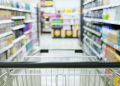 Vemos una imagen de un carrito de compras entre góndolas de supermercado, en relación con el diseño de punto de venta.