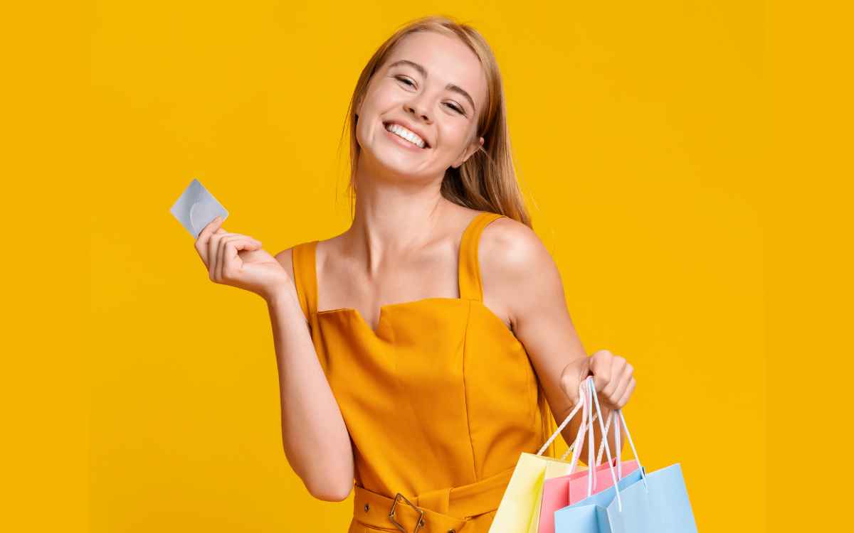 Vemos una persona con bolsas de compra sonriendo y sosteniendo su tarjeta de cliente frecuente.